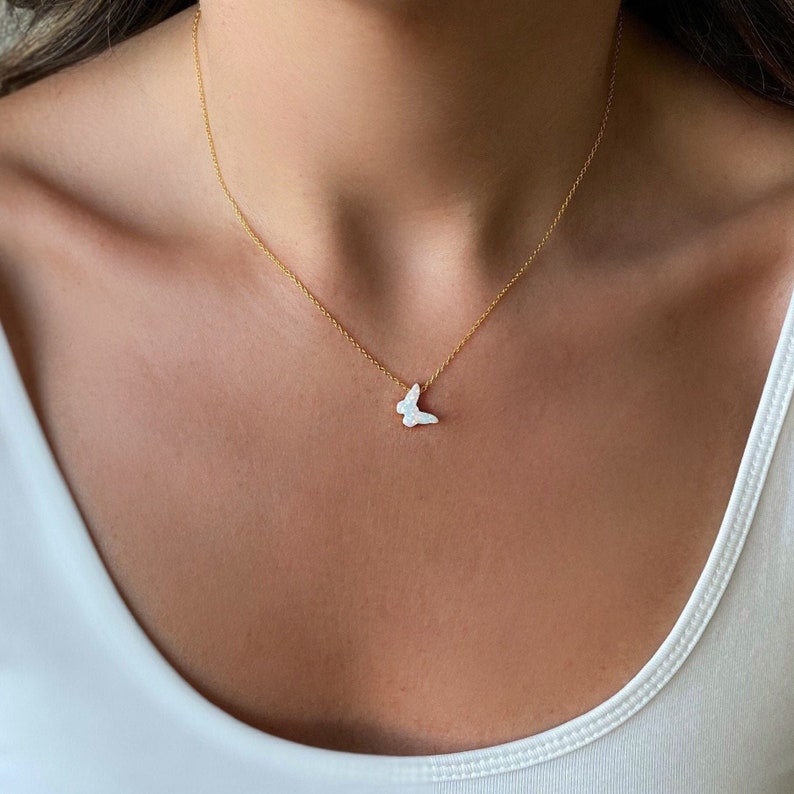 May include: A delicate gold chain necklace with a white butterfly pendant. The butterfly is made of a pearlescent material.