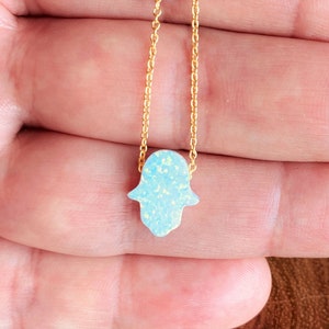 May include: A gold chain necklace with a blue opal hamsa hand charm.