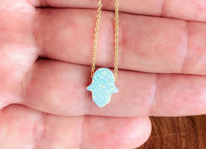 May include: A gold chain necklace with a blue opal hamsa hand charm.