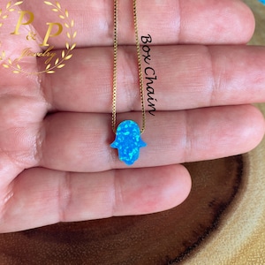 May include: A delicate gold chain necklace with a blue opal hamsa hand charm. The chain is a box chain style. The hamsa hand is a symbol of protection and good luck.