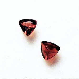 May include: Two triangular red gemstones with a faceted cut.