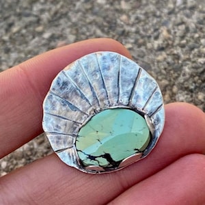 May include: A silver pendant with a green turquoise stone set in a sunburst design.