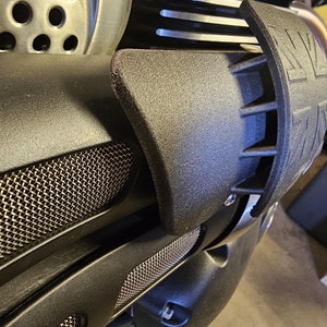 Könnte beinhalten: Nahaufnahme eines schwarzen Motorradmotors mit einem silbernen Auspuffrohr und einem schwarzen Gitter aus Drahtgeflecht. Der Motor hat eine schwarze Kunststoffabdeckung mit einer strukturierten Oberfläche.