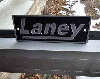 May include: A black metal sign with the word "Laney" in raised silver letters.