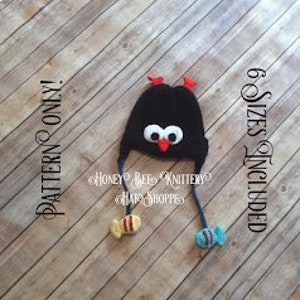 May include: Black crochet hat with red and white bird details and two dangling fish charms. The hat is designed for babies and toddlers. The pattern includes 6 sizes.