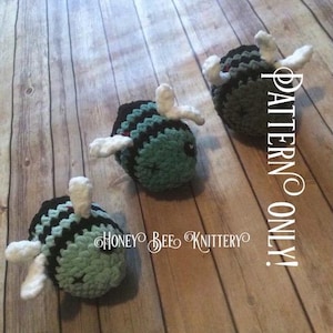 May include: Three handmade crochet bees with black and teal stripes, white wings, and small black eyes. The bees are arranged on a wooden surface. The text "PATTERN ONLY!" and "HONEY BEE KNITTERY" are visible.