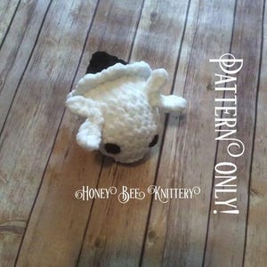 May include: A handmade white crochet creature with black eyes and a black hat. The text "PATTERN ONLY!" is visible on the right side of the image. The text "HONEY BEE KNITTERY" is also visible.