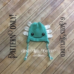May include: A teal blue knitted axolotl hat with white felt accents and black eyes. The hat has a long tail and is available in 6 sizes. The text "Honey Bee Knittery" is printed on the hat.