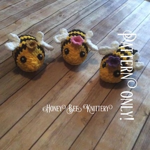 May include: Three handmade crochet bees with yellow and black striped bodies, white wings, and black eyes. One bee has a pink flower, and another has a purple flower. The text "Honey Bee Knittery" and "PATTERN ONLY!" are visible.