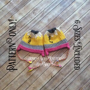 Pode incluir: Dois chapéus de lápis de tricô amarelos, cinzentos, rosa e pretos com bordado preto que diz "Na 2". Os chapéus têm laços longos rosa, amarelos e pretos. O texto "PATTERN ONLY!" e "6 SIZES INCLUDED" está escrito no fundo de madeira.