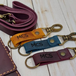 May include: A burgundy leather wallet with two pockets and a matching strap. The wallet has the initials "MCS" embossed on the front. Three matching keychains with the same initials are also included.
