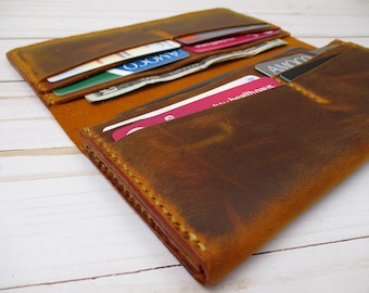 Puede incluir: Una cartera de cuero marrón con múltiples ranuras para tarjetas y un portafolios. La cartera está abierta y se ven varias tarjetas.