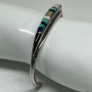 May include: A silver cuff bracelet with a row of inlaid stones in shades of blue, green, white, and black.