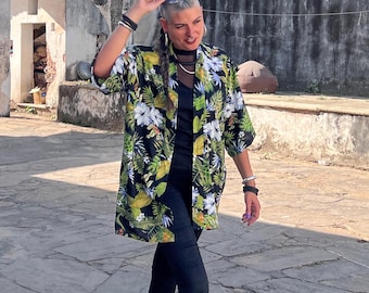 May include: A woman wearing a black and green floral print kimono with black pants and bare feet. She is walking on a stone path in front of a stone wall.