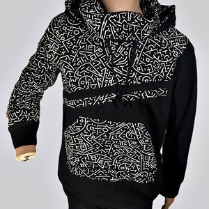 Peut inclure: Sweat-shirt à capuche noir avec un motif géométrique blanc. Le sweat-shirt a une poche kangourou et une capuche à cordon.