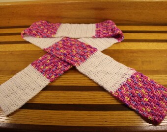 May include: A white and pink crocheted scarf with a multi-colored pattern. The scarf is folded in half and tied in a knot.