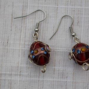 May include: A pair of silver earrings with red, orange, and blue glass beads wrapped in silver wire.