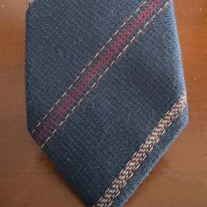 May include: A navy blue tie with a textured weave. The tie features a burgundy stripe down the center and a tan and burgundy stripe along one edge. The tie is angled towards the bottom right corner.