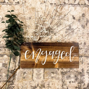 May include: A wooden sign with the word "engaged" written in white calligraphy on a brown background.
