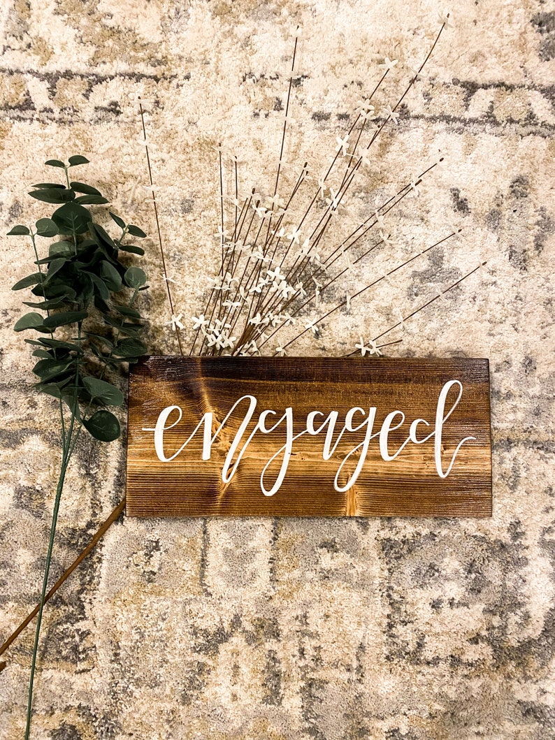 May include: A wooden sign with the word "engaged" written in white calligraphy on a brown background.