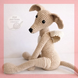 May include: A beige crochet dog toy with long ears, a black nose, and black eyes. The toy features small white wings on its back and a white patch on its chest. A circular graphic in the corner contains the text PDF PATTERN CROCHET.