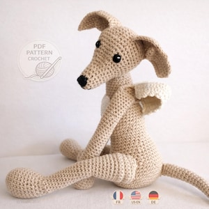 Könnte beinhalten: Eine beige gehäkelte Hundefigur mit langen Ohren, einer schwarzen Nase und schwarzen Augen. Der Hund hat kleine weiße Flügel am Rücken. Eine kreisförmige Grafik in der oberen linken Ecke enthält den Text PDF PATTERN CROCHET mit einem Garnsymbol.