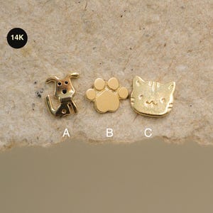 May include: Three small, gold-colored charms in the shape of a dog, a paw print, and a cat. The charms are labeled A, B, and C. The upper left corner has a black circle with the text "14K".