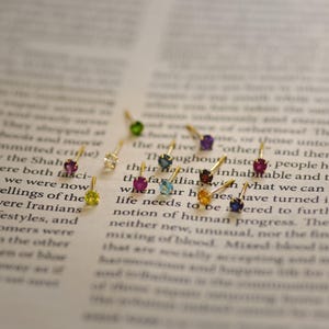May include: Assortment of colorful gemstone earrings with gold settings. The earrings are displayed on a page of a book.