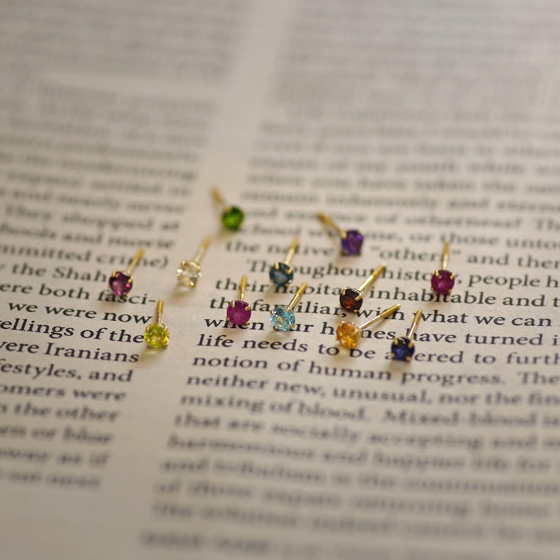 May include: Assortment of colorful gemstone earrings with gold settings. The earrings are displayed on a page of a book.