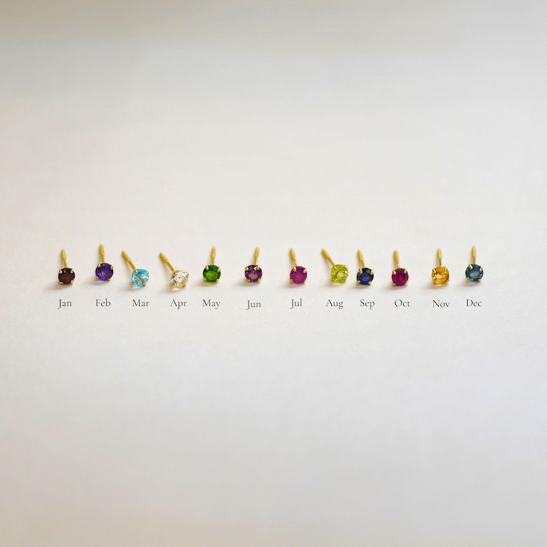 May include: Twelve gold stud earrings with different colored gemstones, representing each month of the year. January is garnet, February is amethyst, March is aquamarine, April is diamond, May is emerald, June is alexandrite, July is ruby, August is peridot, September is sapphire, October is opal, November is citrine, and December is blue topaz.