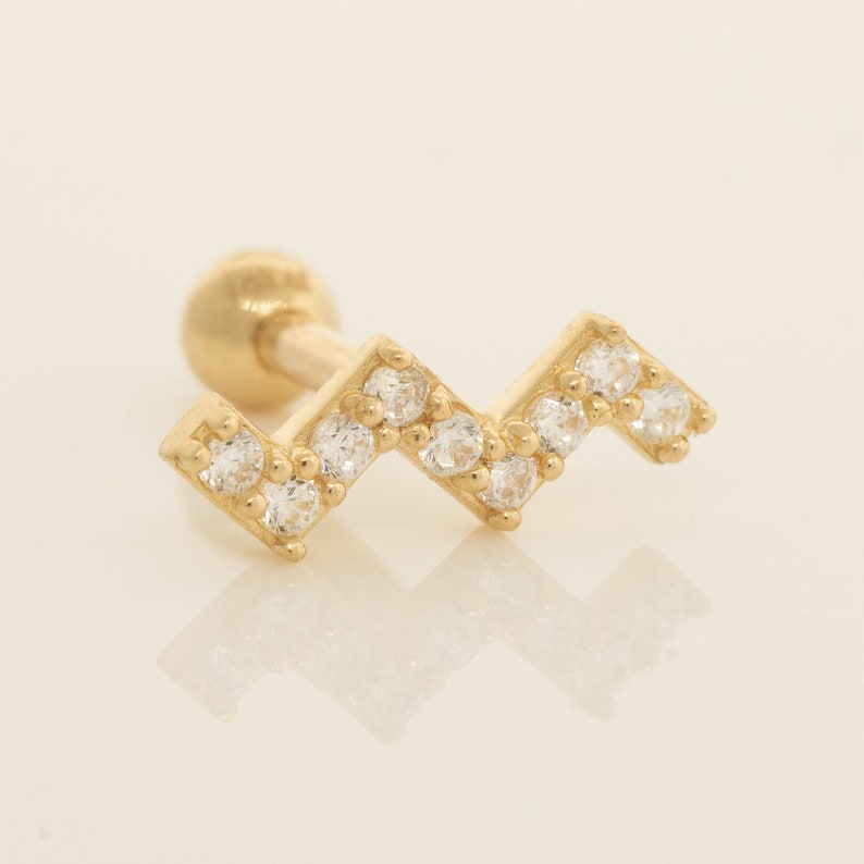 K&ouml;nnte beinhalten: Goldener Ohrstecker mit Zickzack-Design, besetzt mit klaren Zirkonia-Steinen.