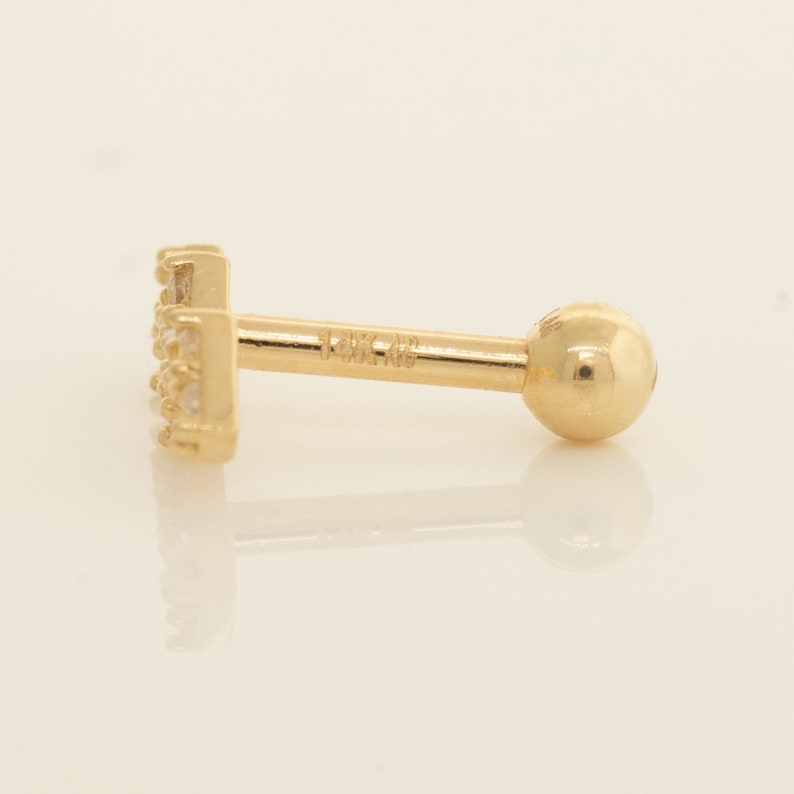 K&ouml;nnte beinhalten: Ein goldener Barren-Ohrstecker mit einer Reihe kleiner, klarer Zirkonia-Steine. Der Ohrstecker ist mit "14K 48" gekennzeichnet.