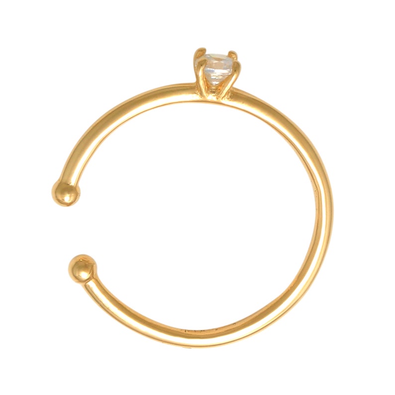 May include: A gold ring with a small clear gemstone on top. The ring is open and has rounded ends.