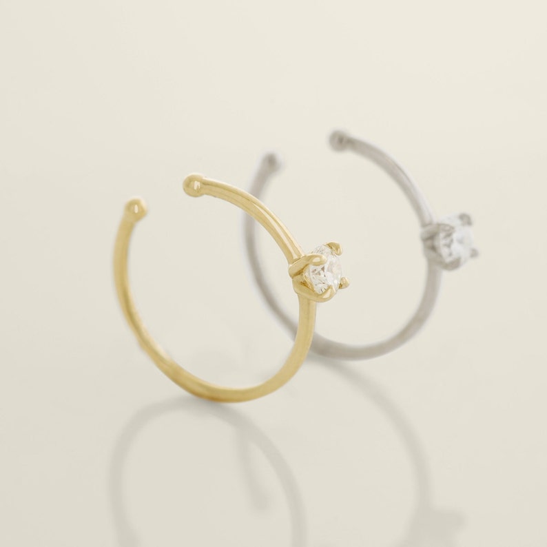 May include: Two ear cuffs with a single clear gemstone on each. One cuff is gold and the other is silver.