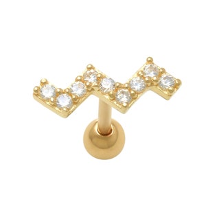 K&ouml;nnte beinhalten: Goldfarbener K&ouml;rperschmuck mit einem klaren Kristall-Zickzack-Muster. Der Schmuck ist ein Knorpel-Ohrring mit einem Kugel-Stift.