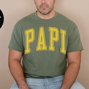 May include: A green t-shirt with the word "PAPI" printed in yellow on the front.