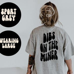 Pode incluir: Uma camiseta cinza com o texto "DIBS ON THE MINER" impresso em preto nas costas. O texto está em uma fonte retrô, com formato de bolha.
