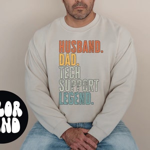Könnte beinhalten: Ein weißer Pullover mit dem Text "Husband. Dad. Tech Support Legend." in einer Vintage-Schriftart mit orange, gelben und blauen Farben.