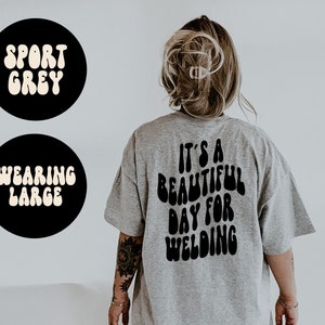 May include: A gray t-shirt with the text "It's a beautiful day for welding" printed on the back in black, retro-style lettering.