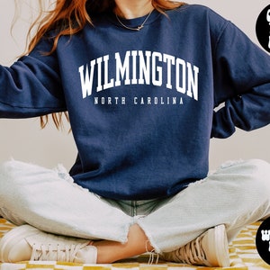 May include: A navy blue sweatshirt with the text "WILMINGTON NORTH CAROLINA" in white. The model is wearing a large size.