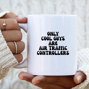 May include: White ceramic mug with black text that reads "Only cool guys are air traffic controllers".