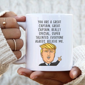 Puede incluir: Taza de caf&eacute; de cer&aacute;mica blanca con una imagen de dibujos animados de Donald Trump y el texto "YOU ARE A GREAT CAPTAIN. GREAT CAPTAIN. REALLY SPECIAL. SUPER TALENTED. EVERYONE AGREES. BELIEVE ME."