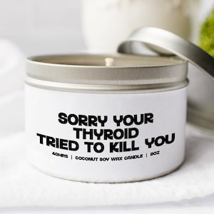 May include: A white 8-ounce candle in a silver tin with the text "SORRY YOUR THYROID TRIED TO KILL YOU." The candle is made of coconut soy wax and has a silver lid. The candle is on a white surface.