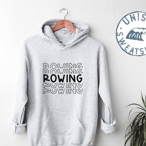 Puede incluir: Sudadera gris unisex con un gráfico negro que dice "ROWING" repetido en un diseño apilado y en capas.