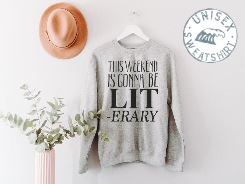 May include: Gray sweatshirt with the text "This weekend is gonna be LIT -ERARY" printed on the front. The sweatshirt is hanging on a hanger against a white wall.