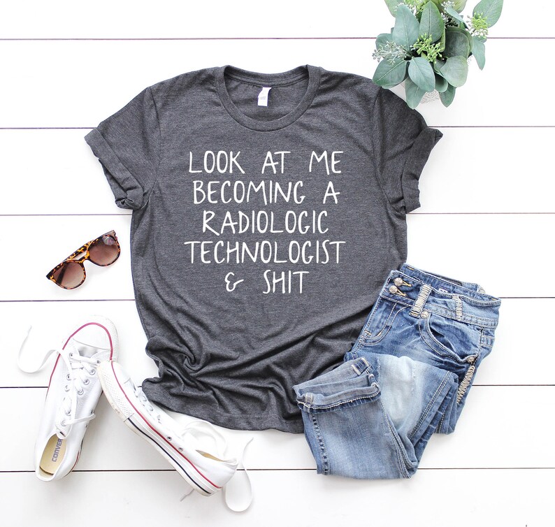 May include: A dark gray t-shirt with the text "LOOK AT ME BECOMING A RADIOLOGIC TECHNOLOGIST & SHIT" printed in white.