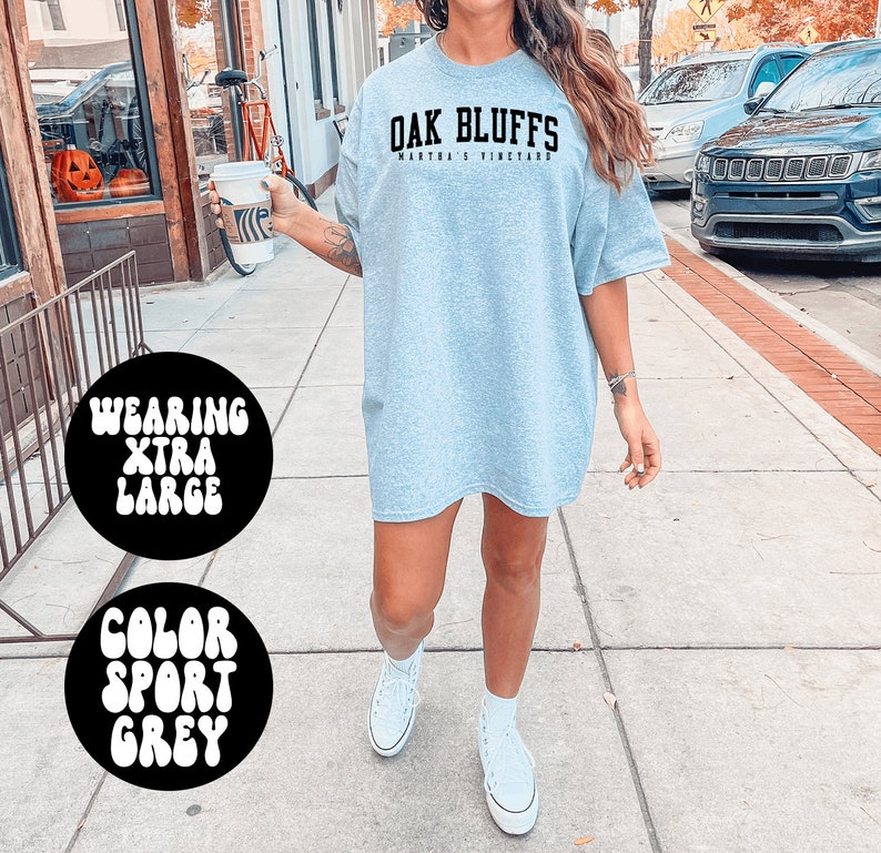 May include: A gray oversized t-shirt with the text "Oak Bluffs Martha's Vineyard" printed on the front. The model is wearing the shirt with white sneakers.