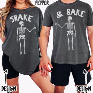 Może przedstawiać: Dwie koszulki w kolorze pieprzowym z grafiką szkieletu. Lewa koszulka ma napis SHAKE nad szkieletem, a prawa koszulka ma napis & BAKE nad szkieletem. Obie koszulki mają okrągły dekolt i krótkie rękawy.