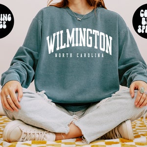 May include: A blue sweatshirt with the text "WILMINGTON NORTH CAROLINA" in white. The model is wearing a large size.