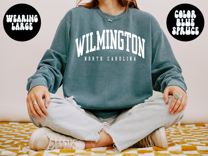 May include: A blue sweatshirt with the text "WILMINGTON NORTH CAROLINA" in white. The model is wearing a large size.